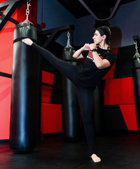Sadaf Aghaei performing a high kick on a heavy bag